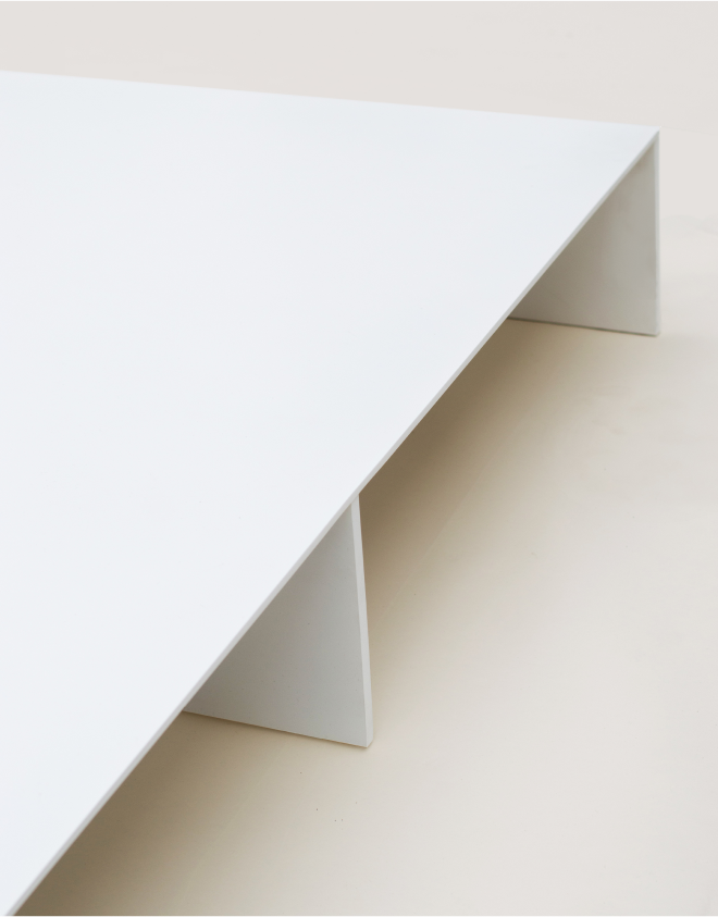 Close-up of a minimalist white bed platform, focusing on the edge of the platform and two of the vertical support panels underneath.