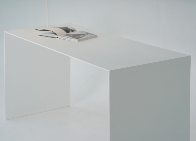 A medium shot of a minimalist white U shape desk. An open book is placed next to the lamp, lying flat on the desk's surface.