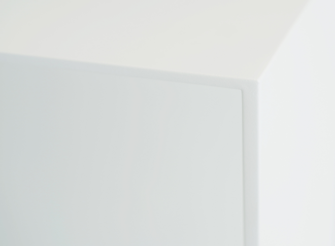A close-up detail of a corner of the white desk table. Thin top forms into slightly thicker leg.