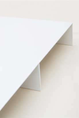 Close-up of a minimalist white bed platform, focusing on the edge of the platform and two of the vertical support panels underneath. 